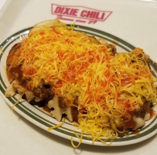 A plate of chili cheese fries topped with melted cheese and drizzled with sauce, served at Dixie Chili.