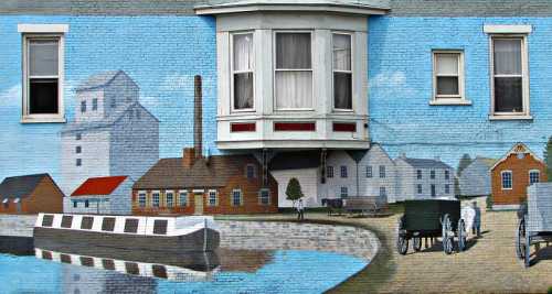 Mural depicting a waterfront scene with houses, a boat, and people walking, set against a blue sky.