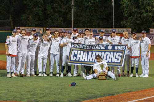 A baseball team celebrates as 2023 Prospect League Champions, holding a banner and trophy on the field.