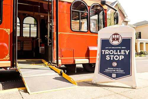 A red trolley at a stop with a sign reading "Trolley Stop" in Chillicothe, Ohio, featuring a ramp for accessibility.