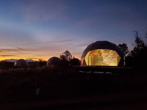 A geodesic dome illuminated at sunset, surrounded by smaller domes and a scenic landscape.