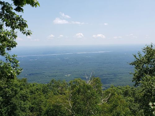 A panoramic view of a lush green landscape under a clear blue sky with scattered clouds.