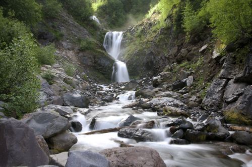 A serene waterfall cascades down rocky cliffs, surrounded by lush greenery and flowing streams.
