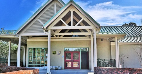 Front view of a modern building with a peaked roof, large windows, and red double doors.