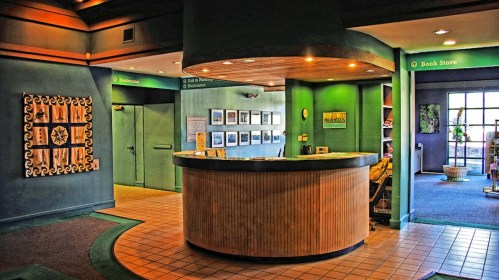 A welcoming reception area with a curved wooden desk, green walls, and framed artwork, leading to a bookstore.