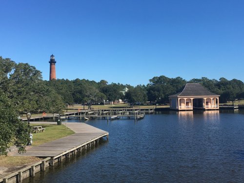 A serene lake view featuring a lighthouse, a gazebo, and wooden docks under a clear blue sky.