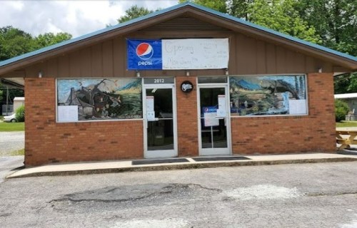 A brick building with a Pepsi sign and a banner, featuring murals on the windows and a gravel parking area.