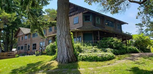A large wooden house surrounded by greenery and trees on a sunny day.