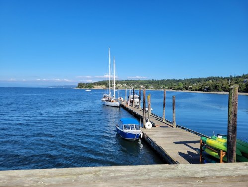 A serene waterfront scene featuring a wooden pier, sailboats, and clear blue skies over calm waters.