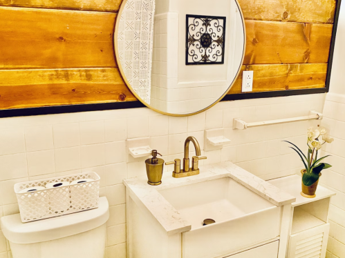 A modern bathroom with a round mirror, wooden wall, sink, and decorative plant.