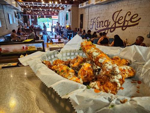 A basket of saucy chicken wings sits on a table, with a lively restaurant atmosphere in the background.
