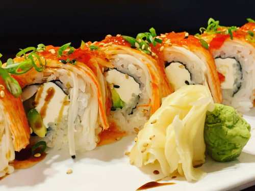 A close-up of sushi rolls topped with spicy sauce, green onions, and served with wasabi and pickled ginger.