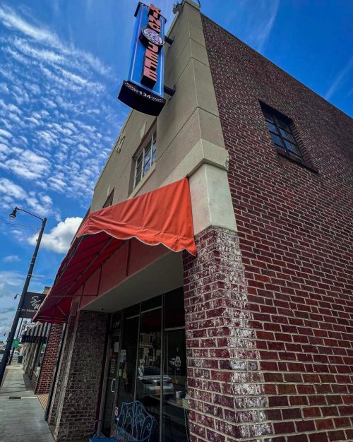 A brick building with a red awning and a sign that reads "Coffee" against a blue sky with clouds.
