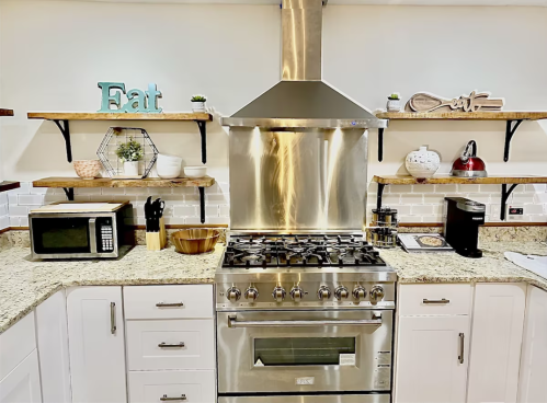 Modern kitchen with stainless steel appliances, granite countertops, and decorative shelves featuring "Eat" signs.