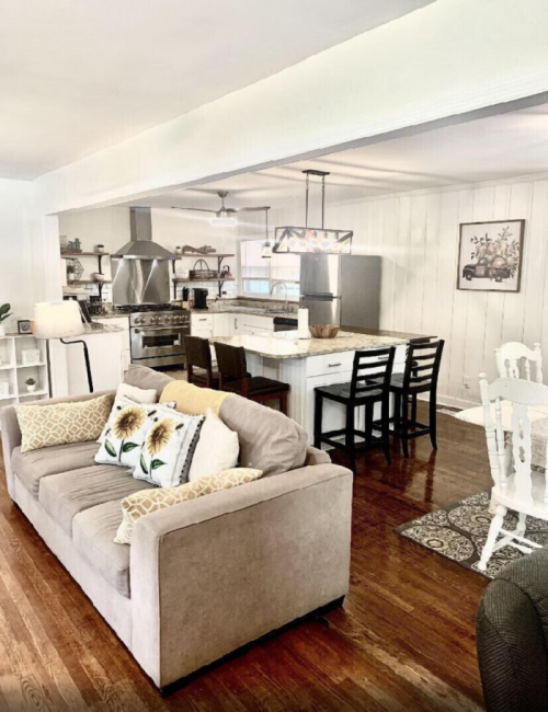 Cozy living room with a sofa, dining area, and modern kitchen featuring wooden floors and bright decor.