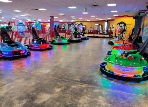 A colorful arcade with bumper cars illuminated by vibrant lights, set in a spacious indoor entertainment area.