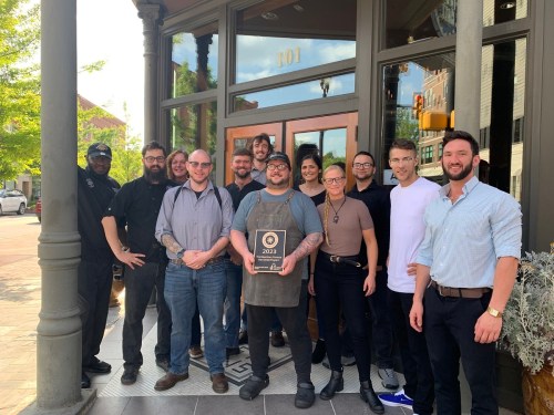 A group of diverse restaurant staff poses proudly outside their establishment, holding an award plaque.