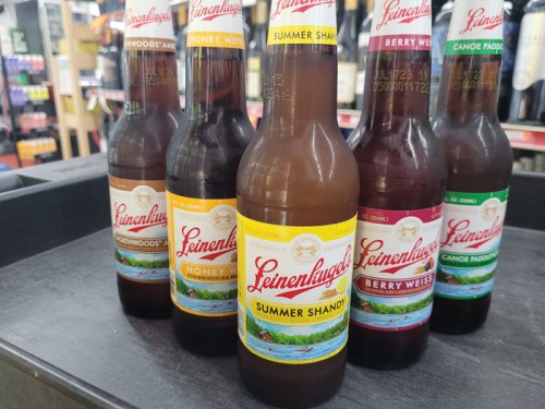 Five bottles of Leinenkugel's beer, including Summer Shandy, Honey Weiss, and Berry Weiss, displayed on a shelf.