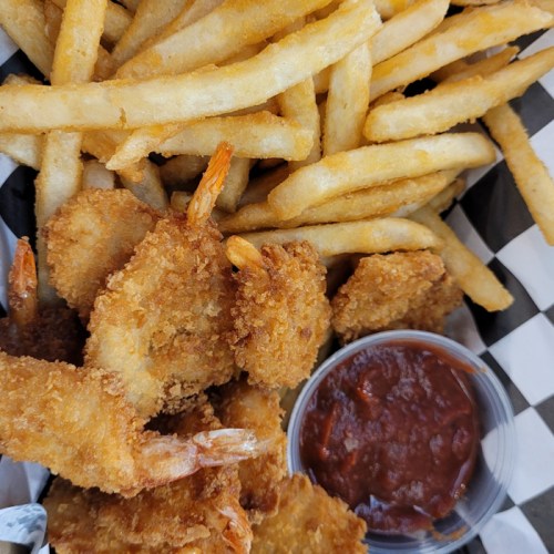 A plate of golden fried shrimp with crispy French fries and a side of dipping sauce.