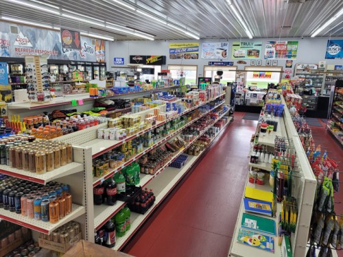 A well-stocked convenience store aisle with various beverages, snacks, and household items on display.