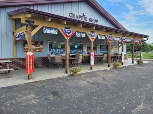 Exterior of Crappie Shop featuring a covered patio, banners, and signage for groceries and fast food.