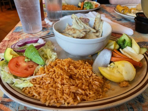 A plate of rice with grilled chicken, fresh vegetables, and a side salad, served in a casual dining setting.