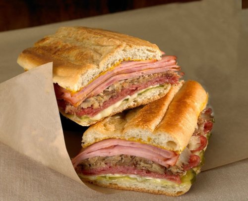 A close-up of a stacked sandwich with layers of meats, cheese, and pickles, served on a toasted hoagie roll.