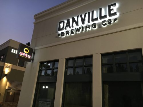Exterior of Danville Brewing Co. building at dusk, featuring illuminated signage and large windows.