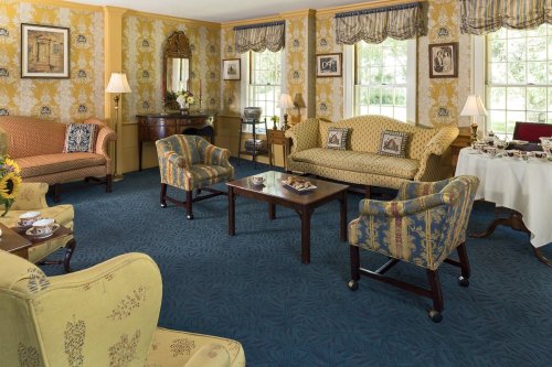 Cozy living room with patterned sofas, armchairs, a coffee table, and floral wallpaper, filled with natural light.