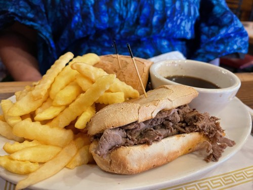 A plate with a beef sandwich, crinkle-cut fries, and a small bowl of dipping sauce.