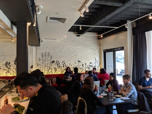 A bustling restaurant interior with diners at tables, featuring a floral mural and bright natural light.