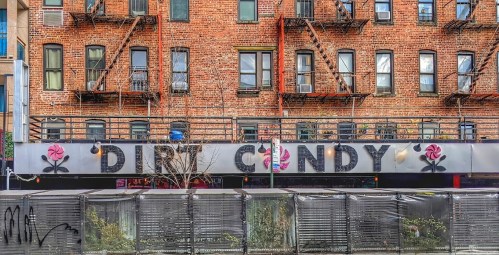 Exterior of a brick building featuring the sign "DIRTY CANDY" with decorative roses and outdoor seating.