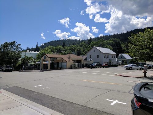 A quiet street scene with buildings, trees, and a blue sky with clouds in a small town.