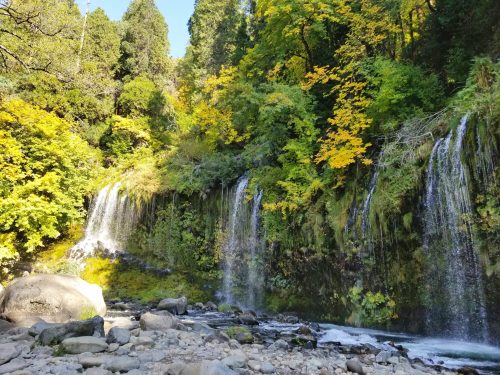 A serene landscape featuring cascading waterfalls surrounded by vibrant autumn foliage and rocky terrain.