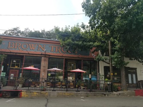 A cozy restaurant named "Brown Trout" with outdoor seating and umbrellas, surrounded by trees on a sunny day.