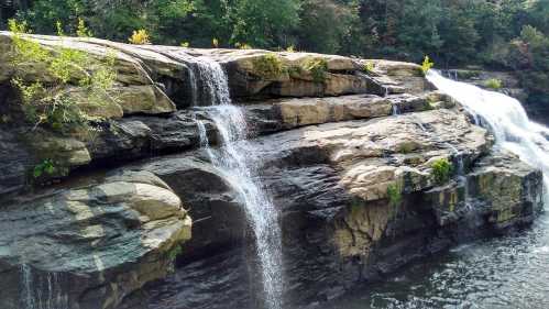 A serene waterfall cascading over rocky cliffs into a calm body of water, surrounded by lush greenery.