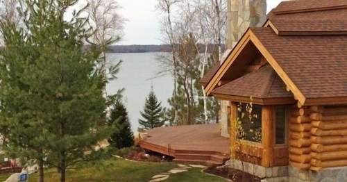 A cozy log cabin by a lake, surrounded by trees and a wooden deck, with a serene water view in the background.