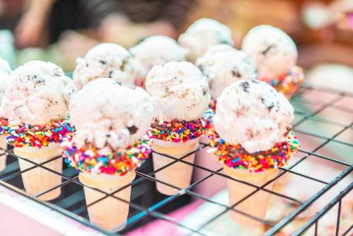 A display of ice cream cones topped with scoops of ice cream and colorful sprinkles on a wire rack.