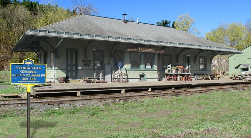 Historic train station with a green exterior, surrounded by grass and trees, featuring a sign for Phoenix Station.