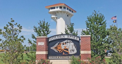 Sign for the Golden Spike Tower and Visitor Center, featuring a tall observation tower and landscaped greenery.