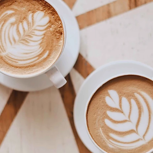 Two cups of latte art with leaf designs, placed on a wooden table.