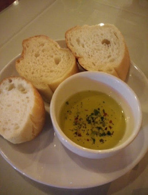 A plate with three pieces of bread and a small bowl of olive oil mixed with herbs and spices.