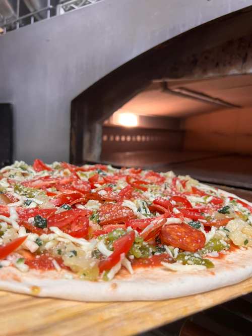 A freshly topped pizza with tomatoes, cheese, and herbs, ready to be baked in a pizza oven.