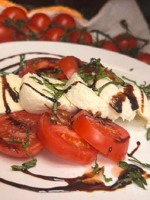 Fresh mozzarella and tomato slices drizzled with balsamic glaze and garnished with basil on a white plate.