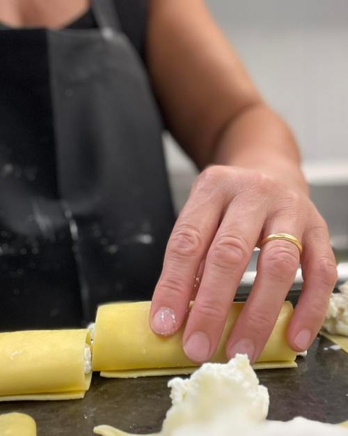 A hand rolls pasta filled with ricotta on a countertop, with flour scattered around.