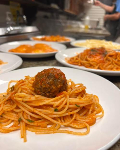 A plate of spaghetti topped with a meatball, with additional pasta dishes in the background.