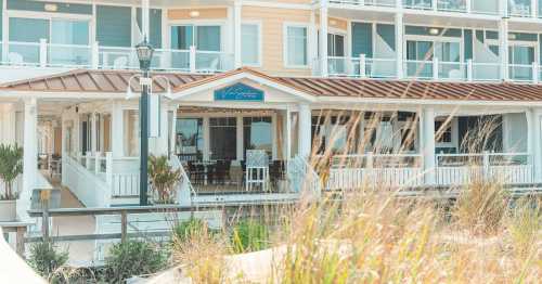 A coastal hotel with multiple balconies, surrounded by tall grass and a clear sky.