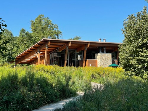 A modern building with a wooden roof, surrounded by lush greenery and a clear blue sky.