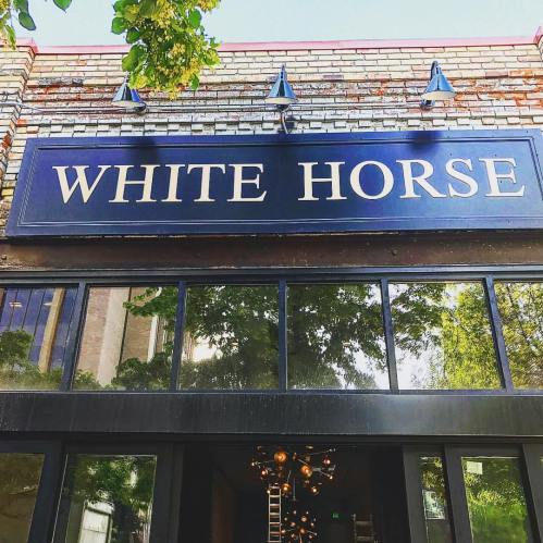 Sign for "White Horse" on a building, with trees reflecting in the glass entrance.