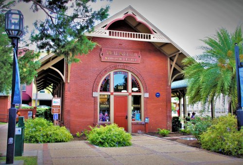 Historic brick building with a large arched window, surrounded by greenery and palm trees. Sign reads "Merritt Island."